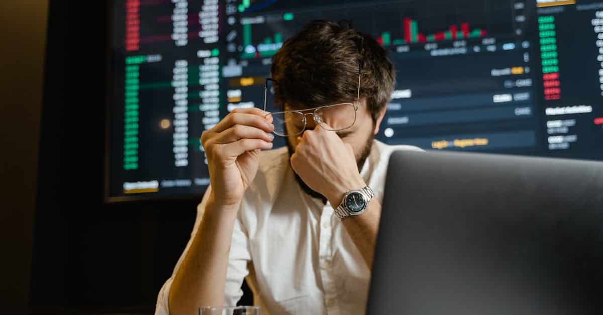 a stressed man looks at stock market data on his computer screen in an office setting